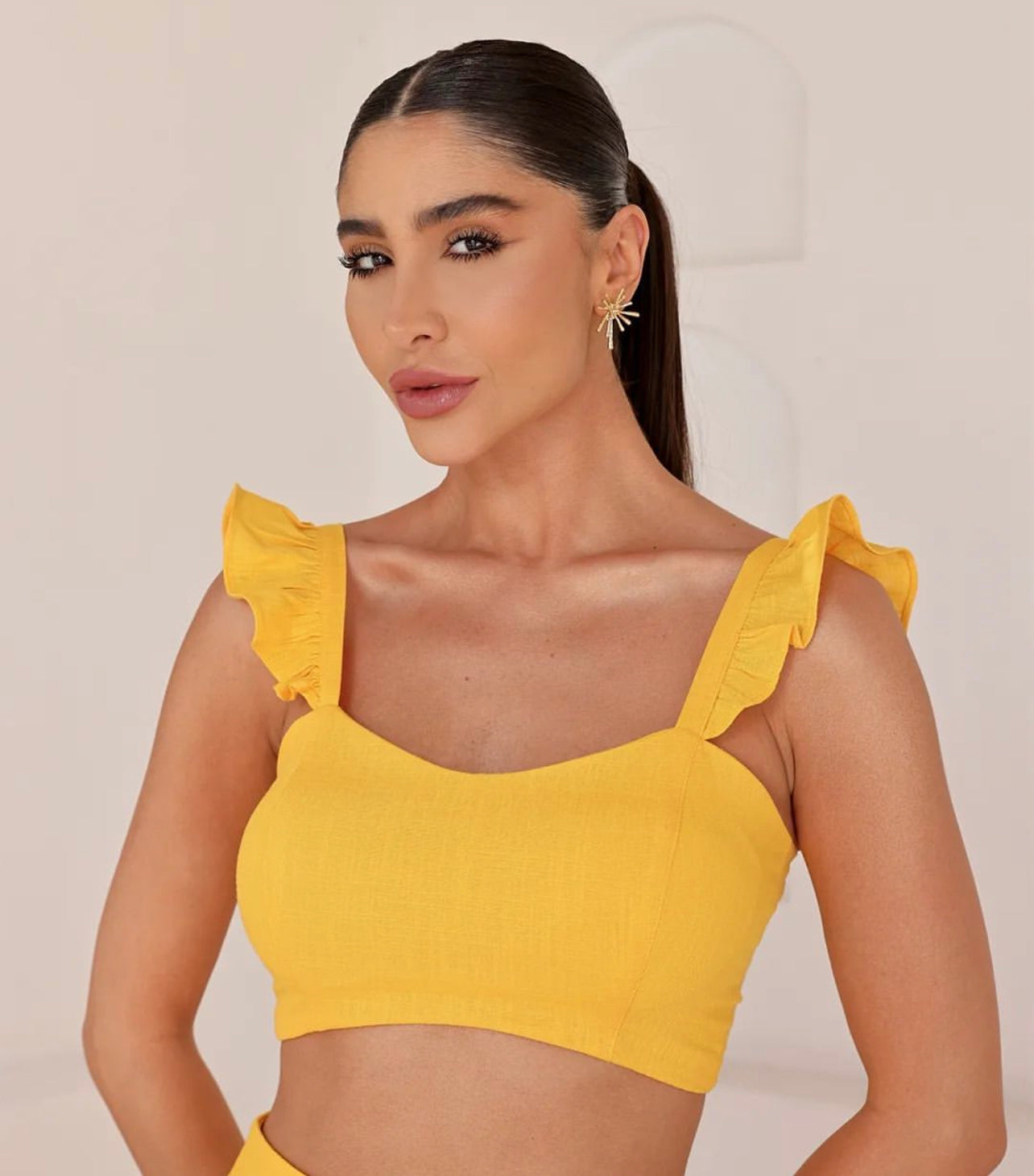 Close-up of yellow ruffled strap cropped top in summer set, worn by model with sleek hair.