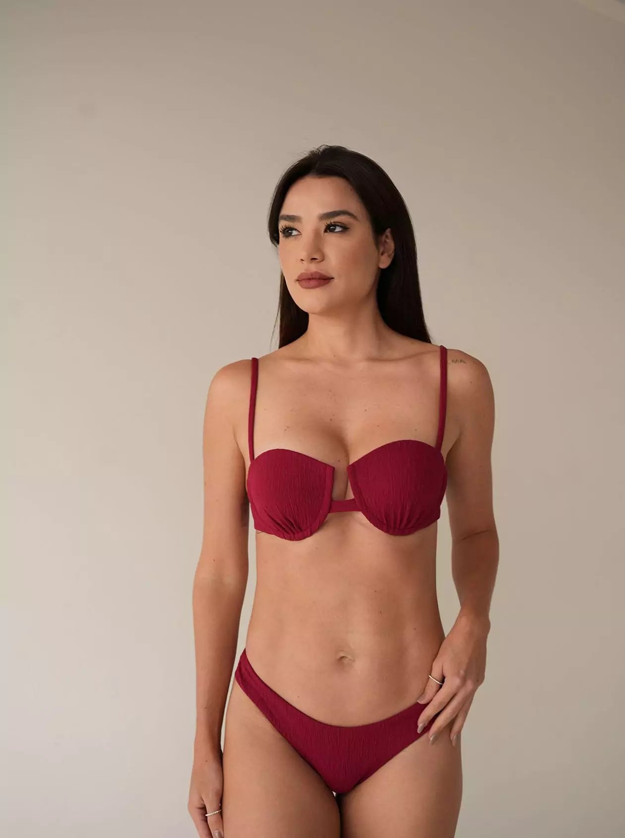 Model in burgundy bikini top and bottom, standing in relaxed neutral setting