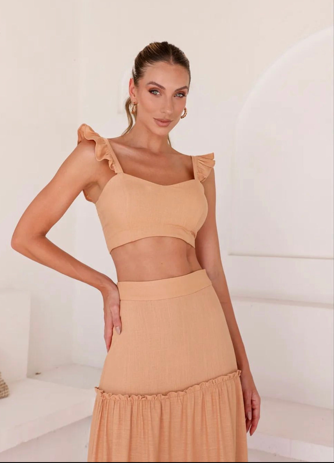 Model wearing beige two-piece set with high-waisted tiered maxi skirt and cropped top, ideal for resortwear.