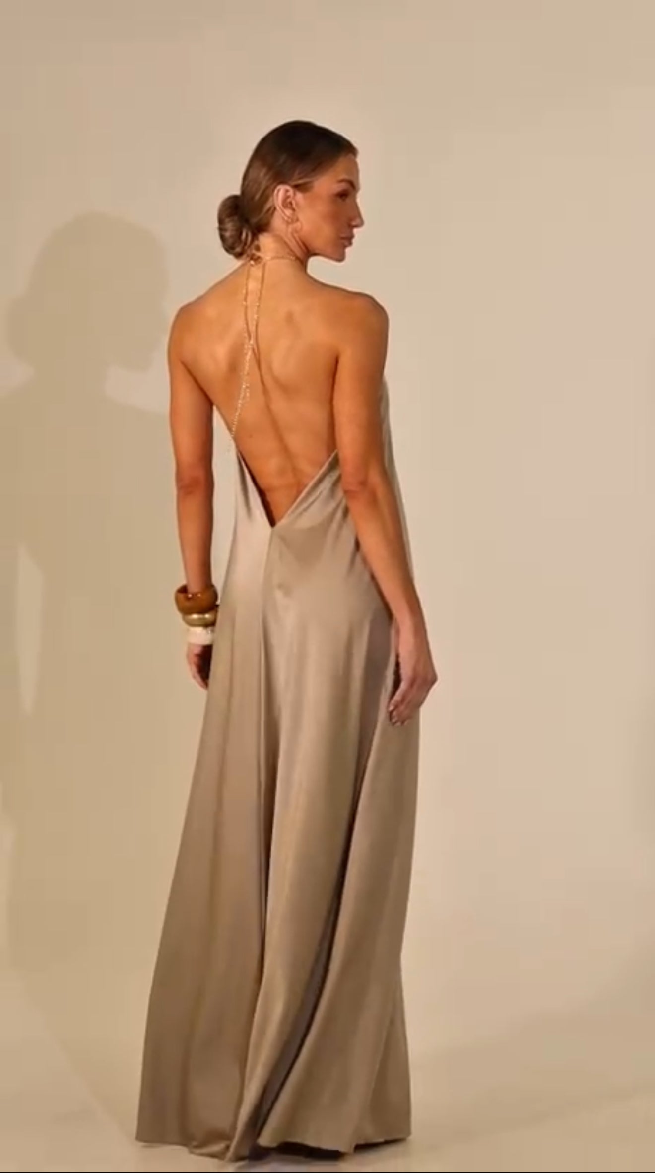 Woman wearing a long, elegant dress with a backless design on a plain background