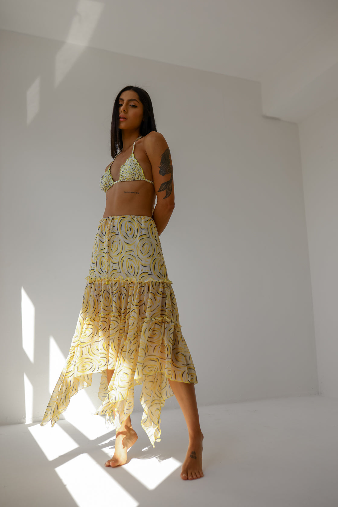A woman wearing a yellow viscose skirt with a floral pattern, posing against a white background.