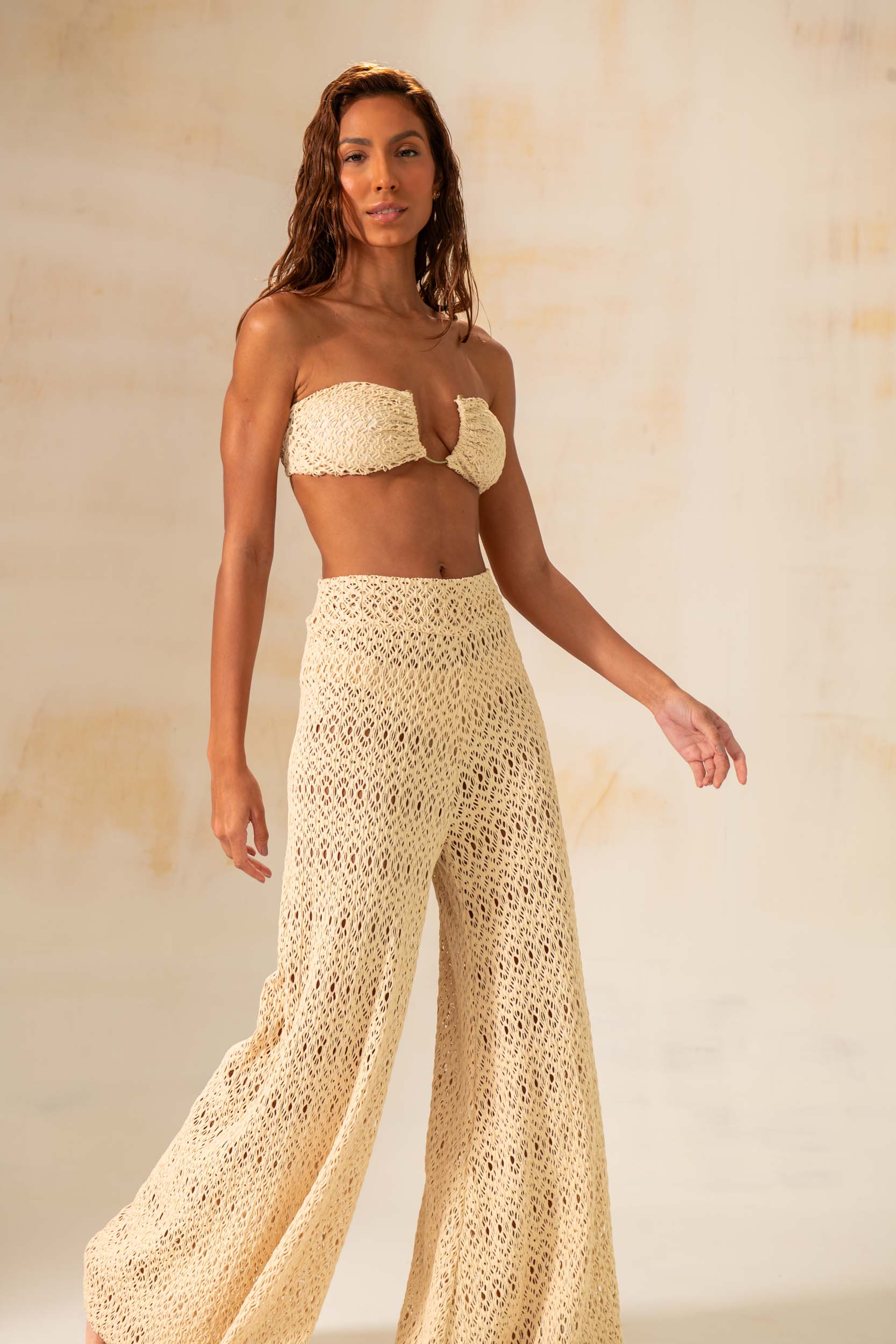 Model wearing handmade crochet wide-leg pants in natural and rust tones, styled as beach cover-up with matching tops.
