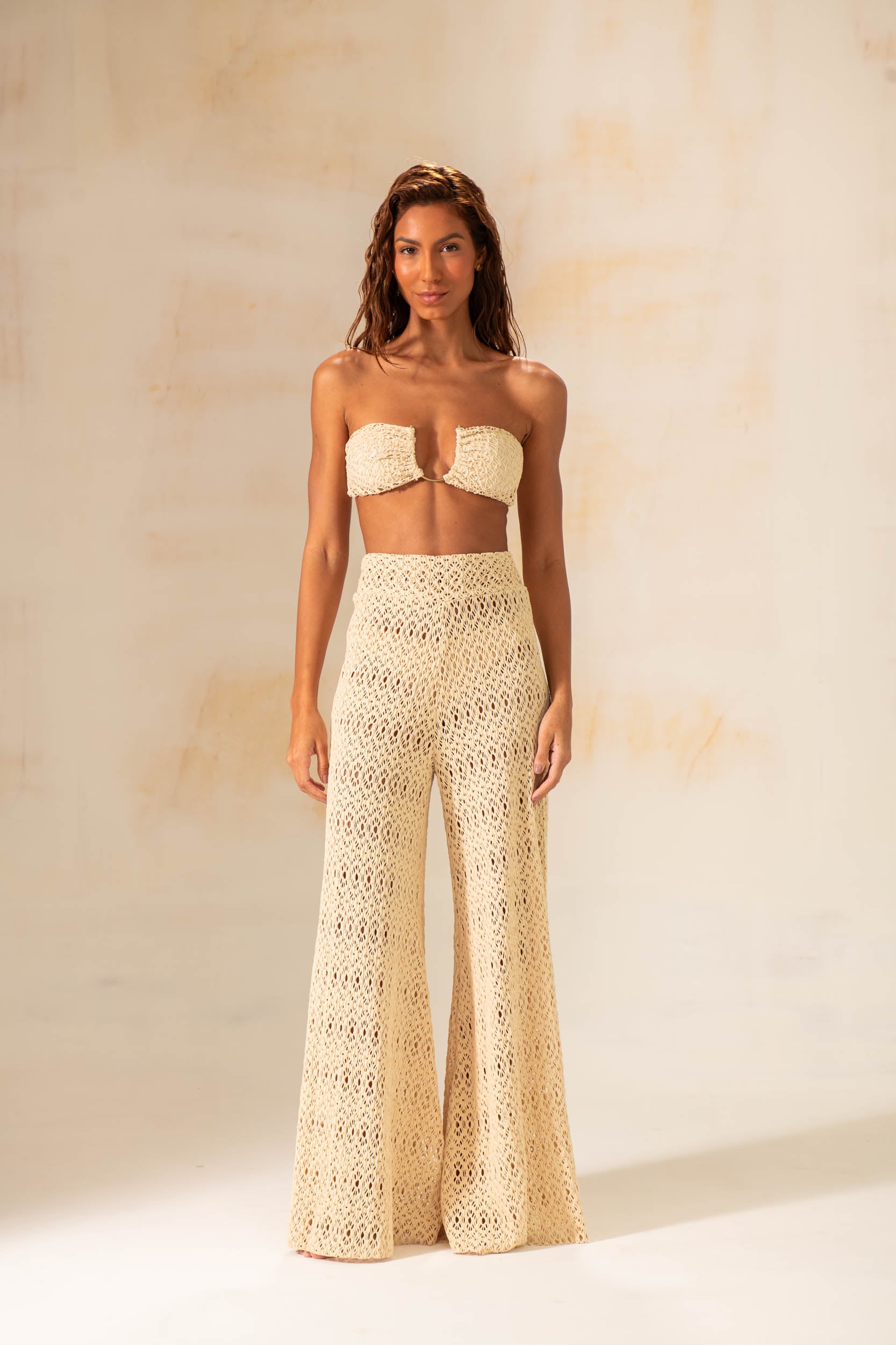 Model wearing handmade crochet wide-leg pants in natural and rust tones, styled as beach cover-up with matching tops.