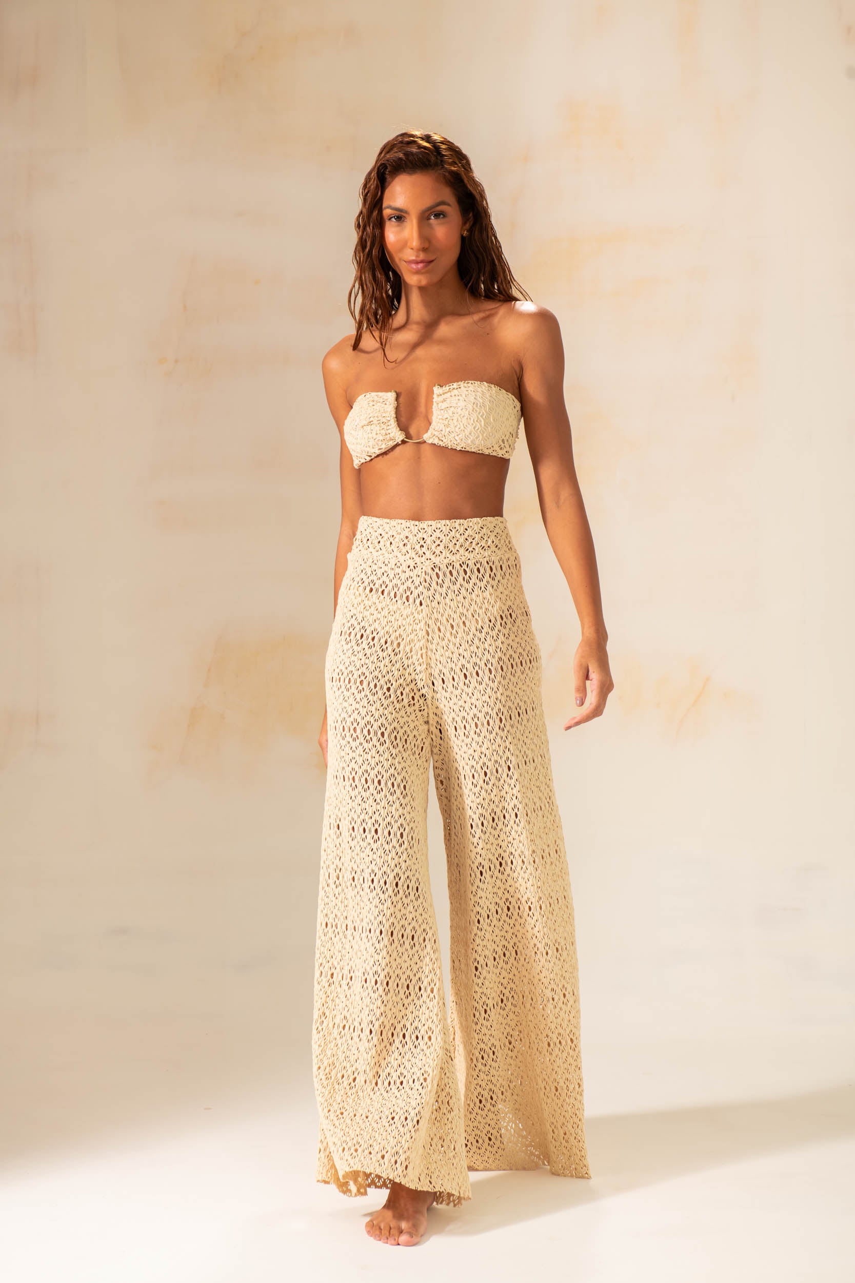 Model wearing handmade crochet wide-leg pants in natural and rust tones, styled as beach cover-up with matching tops.