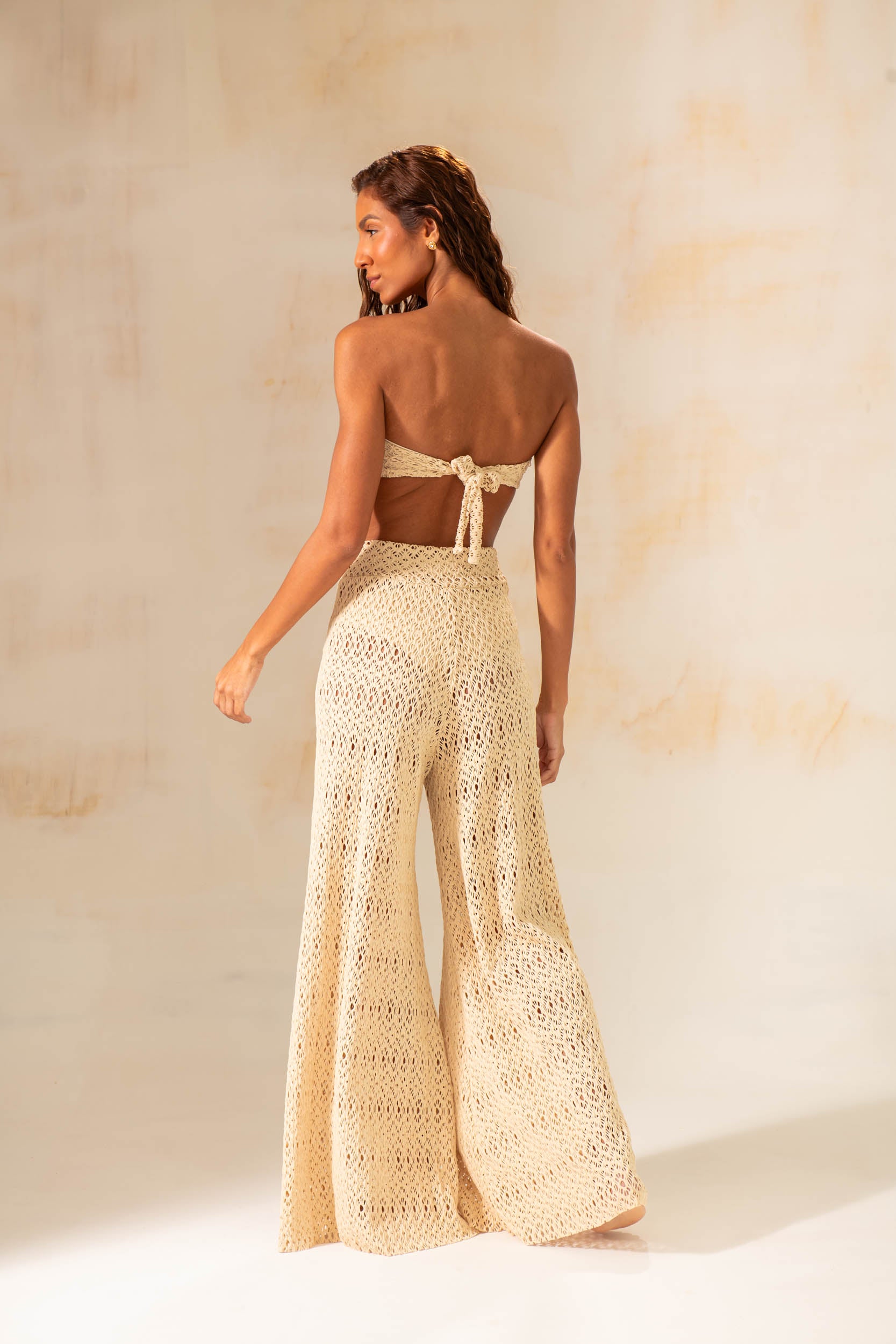 Model wearing handmade crochet wide-leg pants in natural and rust tones, styled as beach cover-up with matching tops.