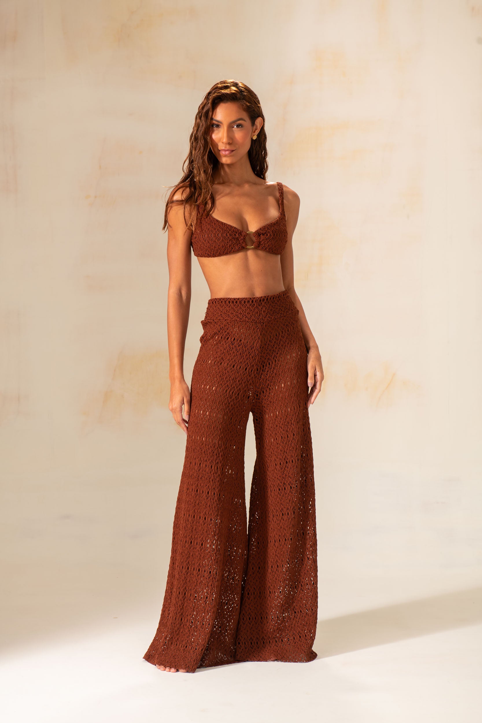 Model wearing handmade crochet wide-leg pants in natural and rust tones, styled as beach cover-up with matching tops.