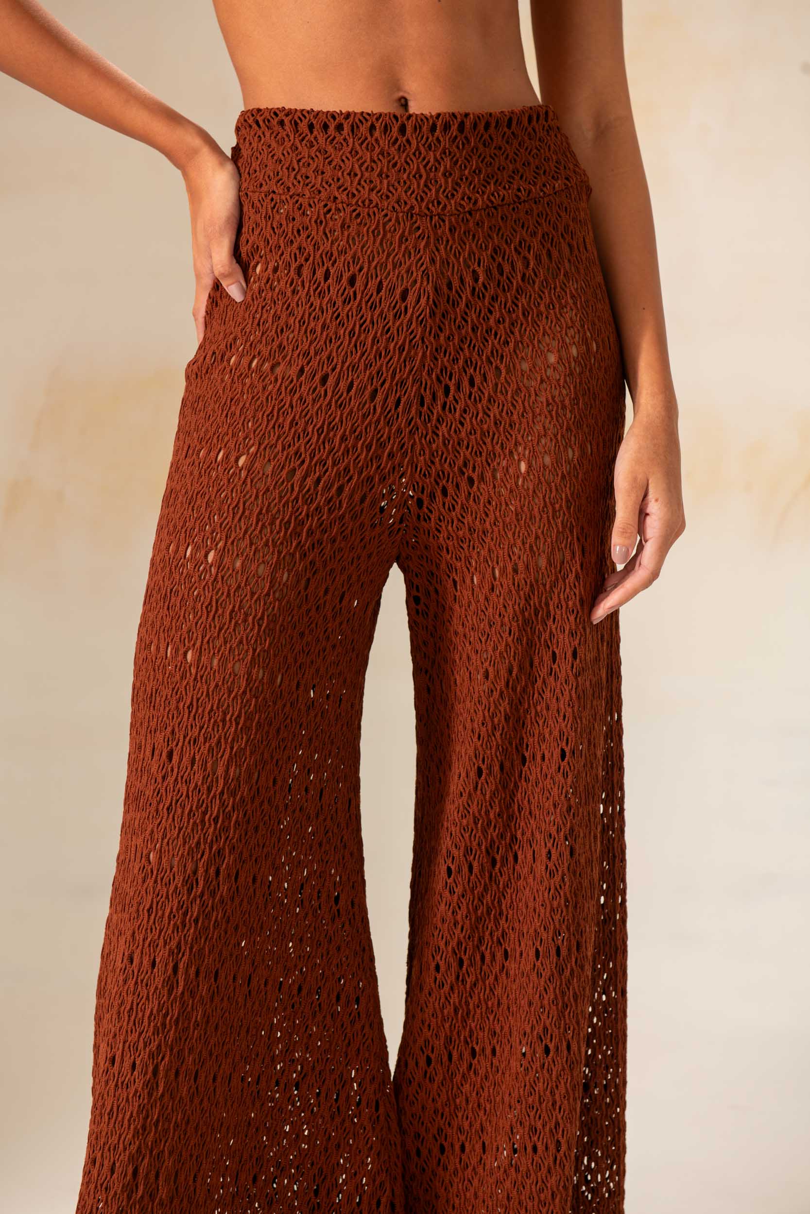 Model wearing handmade crochet wide-leg pants in natural and rust tones, styled as beach cover-up with matching tops.