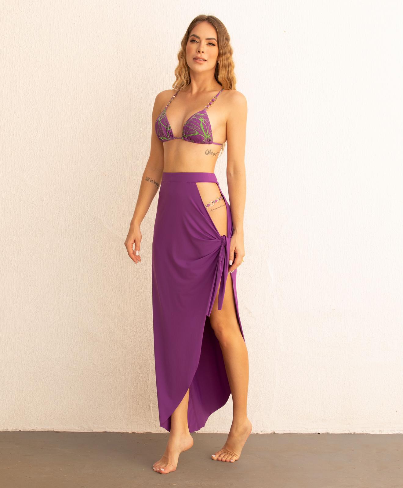 A model wearing a long purple skirt that reaches mid-hip, tied on the side. The skirt features a fluid, light fabric.