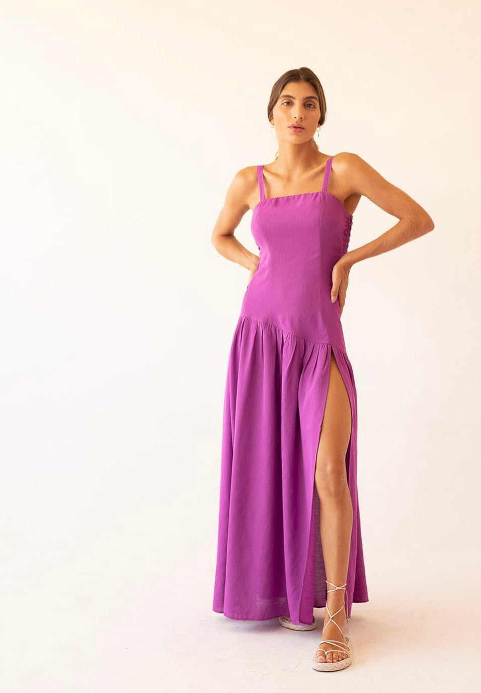 Back view of smocked violet maxi dress with adjustable straps, worn by model with wavy ponytail and neutral sandals.