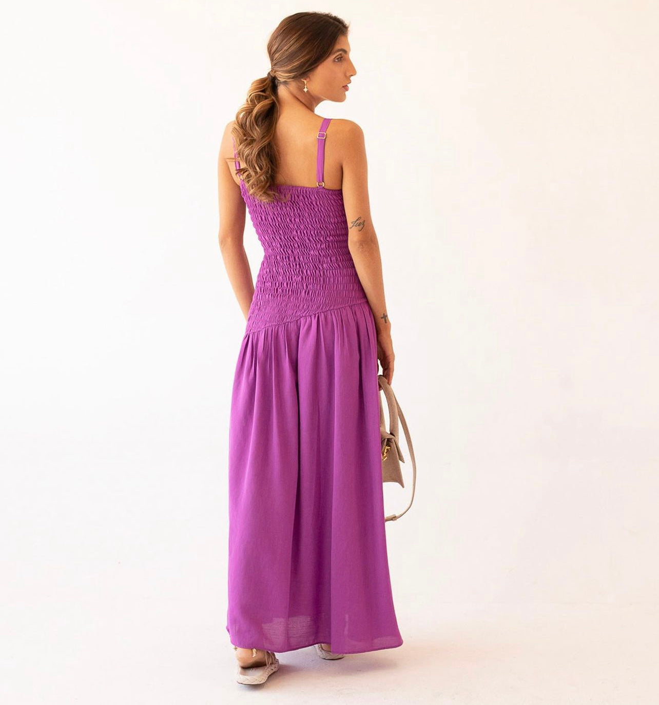 Woman wearing violet maxi dress with side slit and straight neckline, hands on waist, standing against a white background.