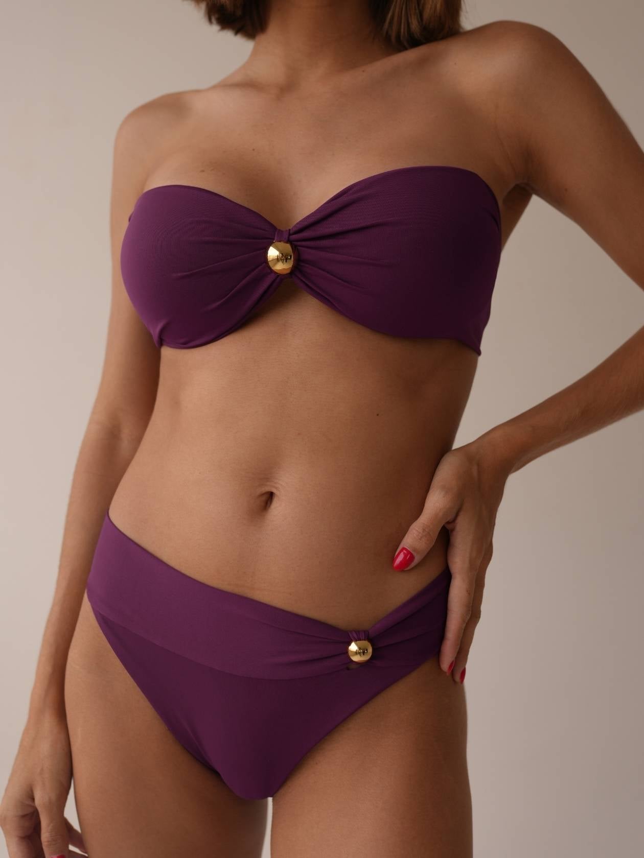 Close-up of bandeau bikini in purple with gold twist detail, soft lighting
