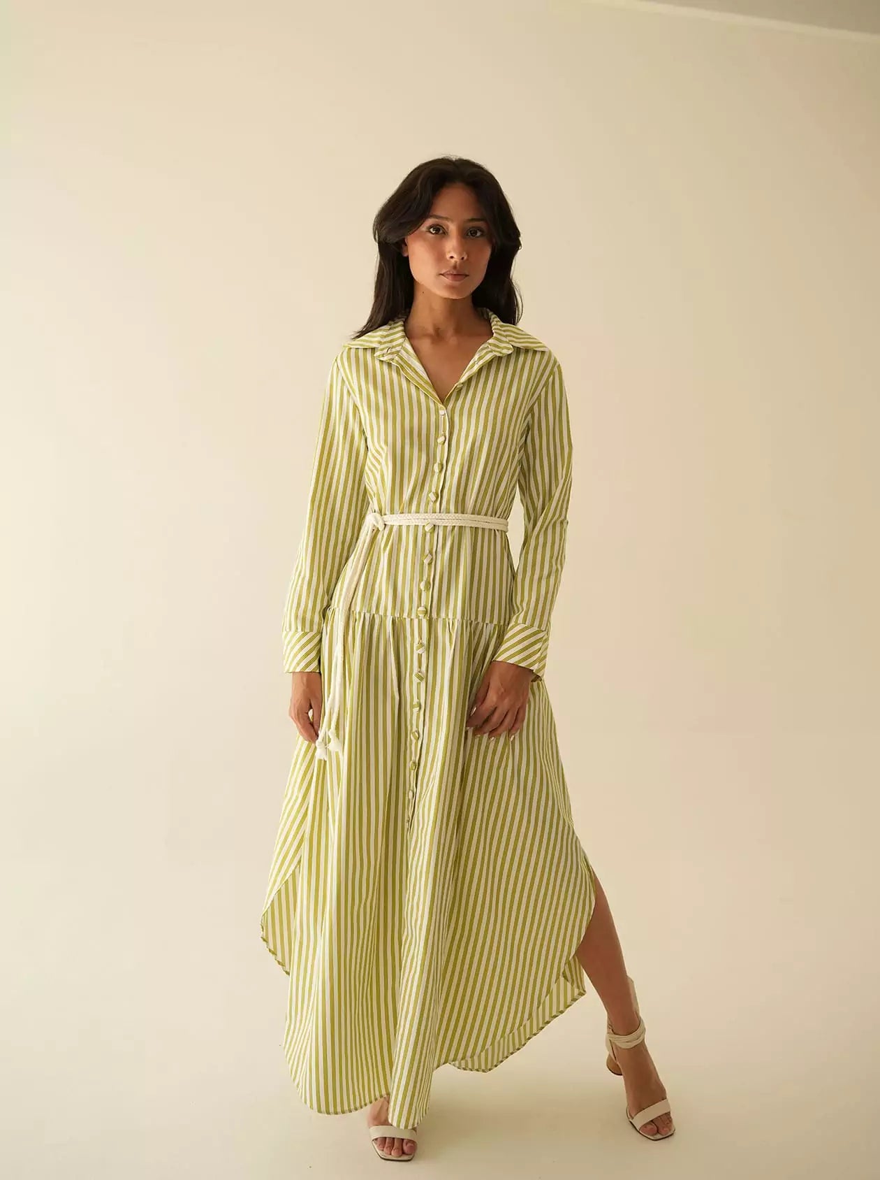 Model wearing a long button-down striped dress with long sleeves, standing front-facing in white heels