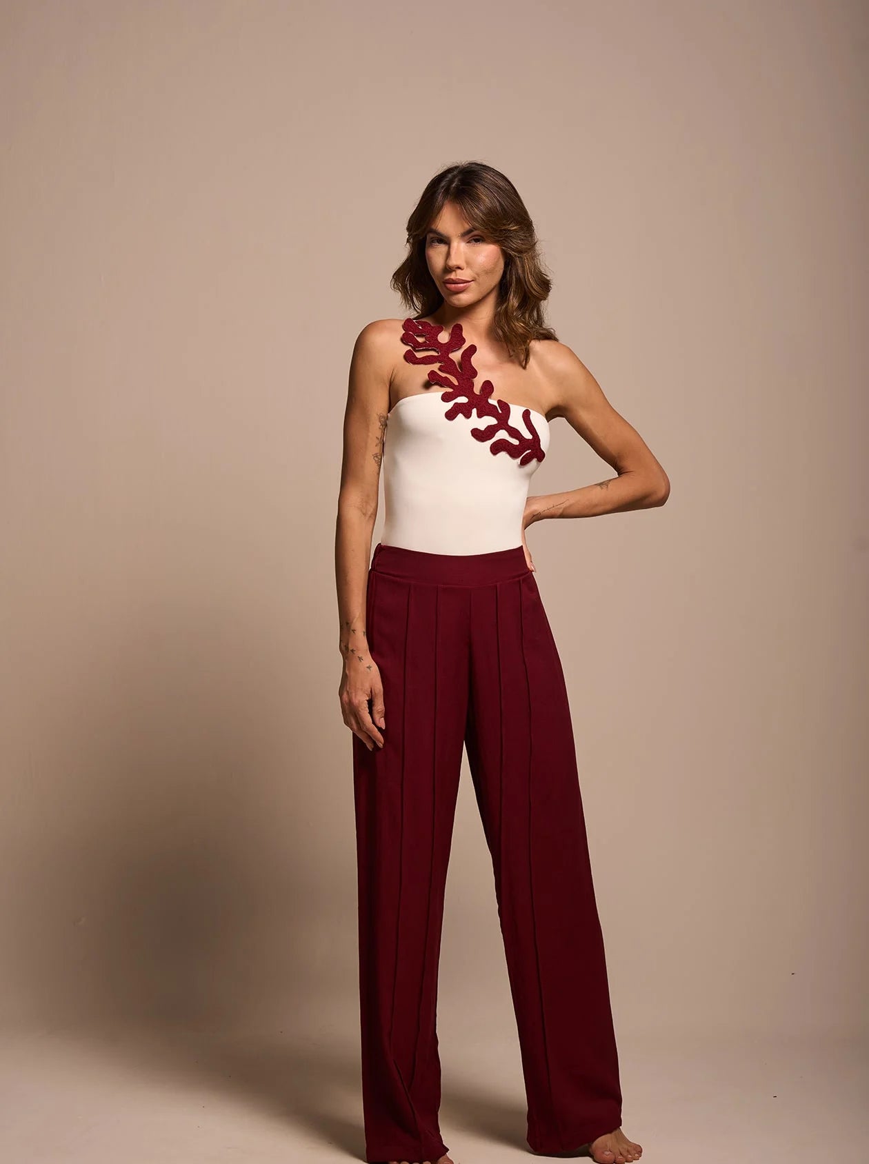 Model wearing ruby wide-leg pants styled with off-white top, elegant studio lighting.
