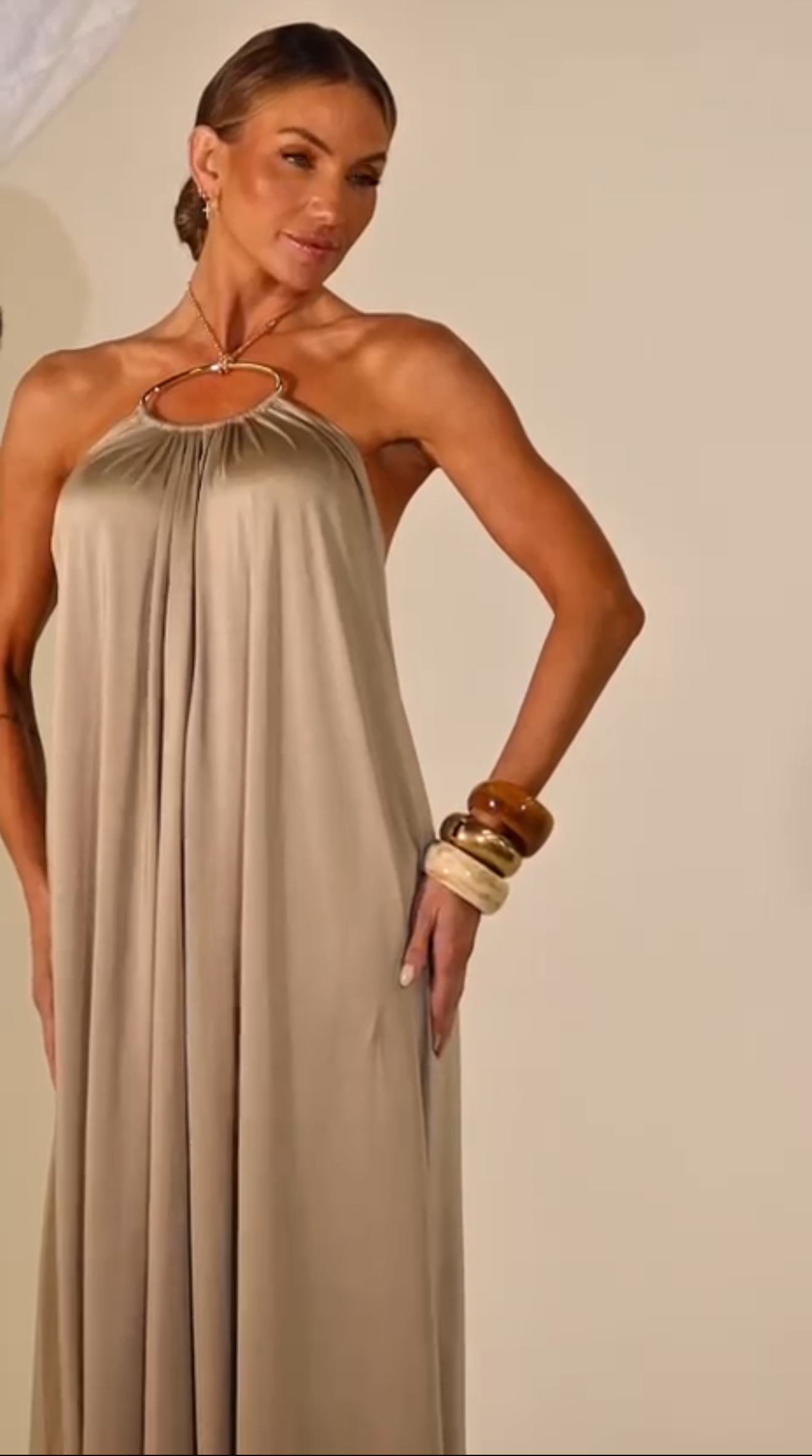 Woman wearing a beige halter neck dress against a plain background