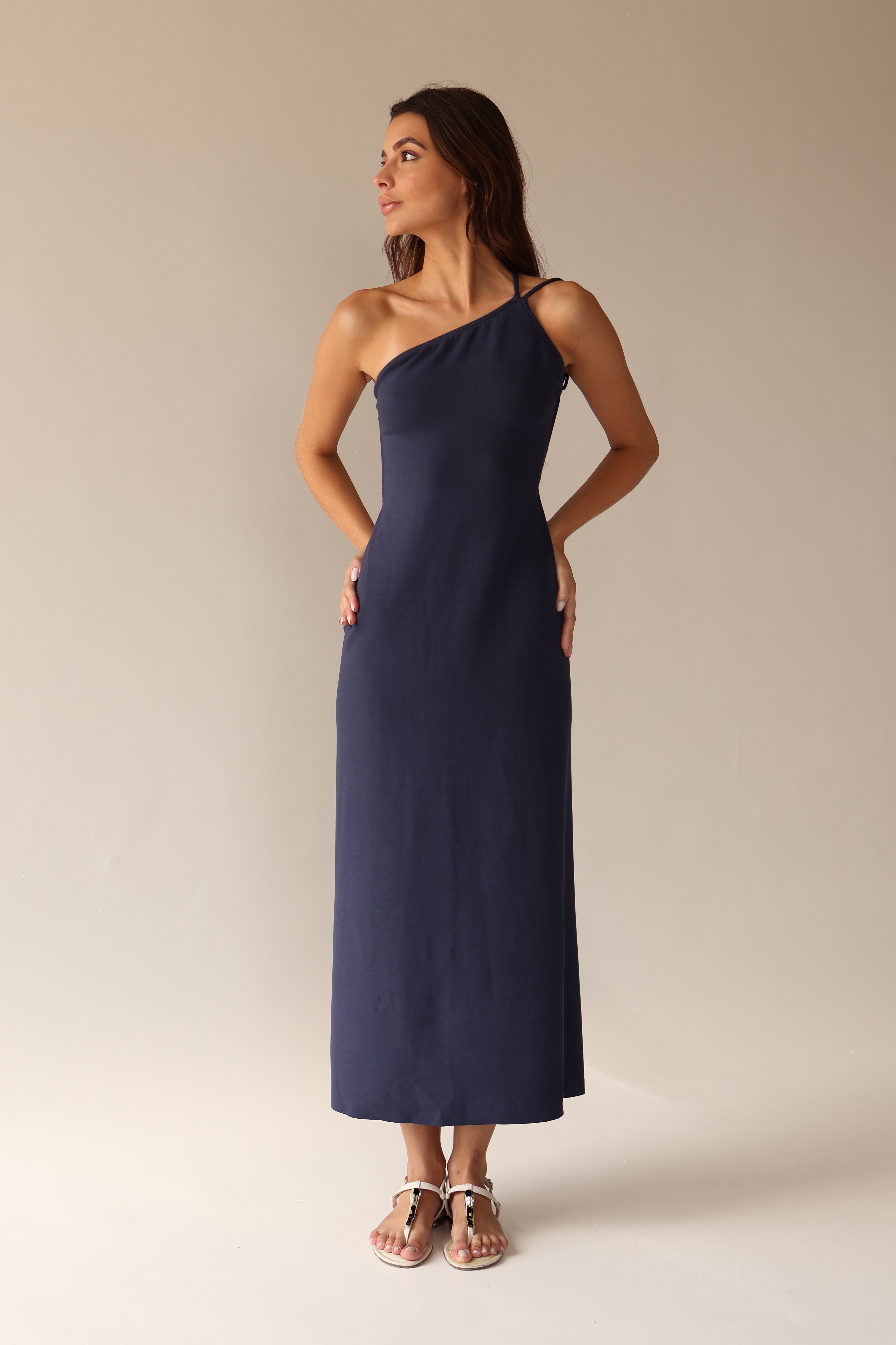Woman wearing a navy one-shoulder dress against a beige background