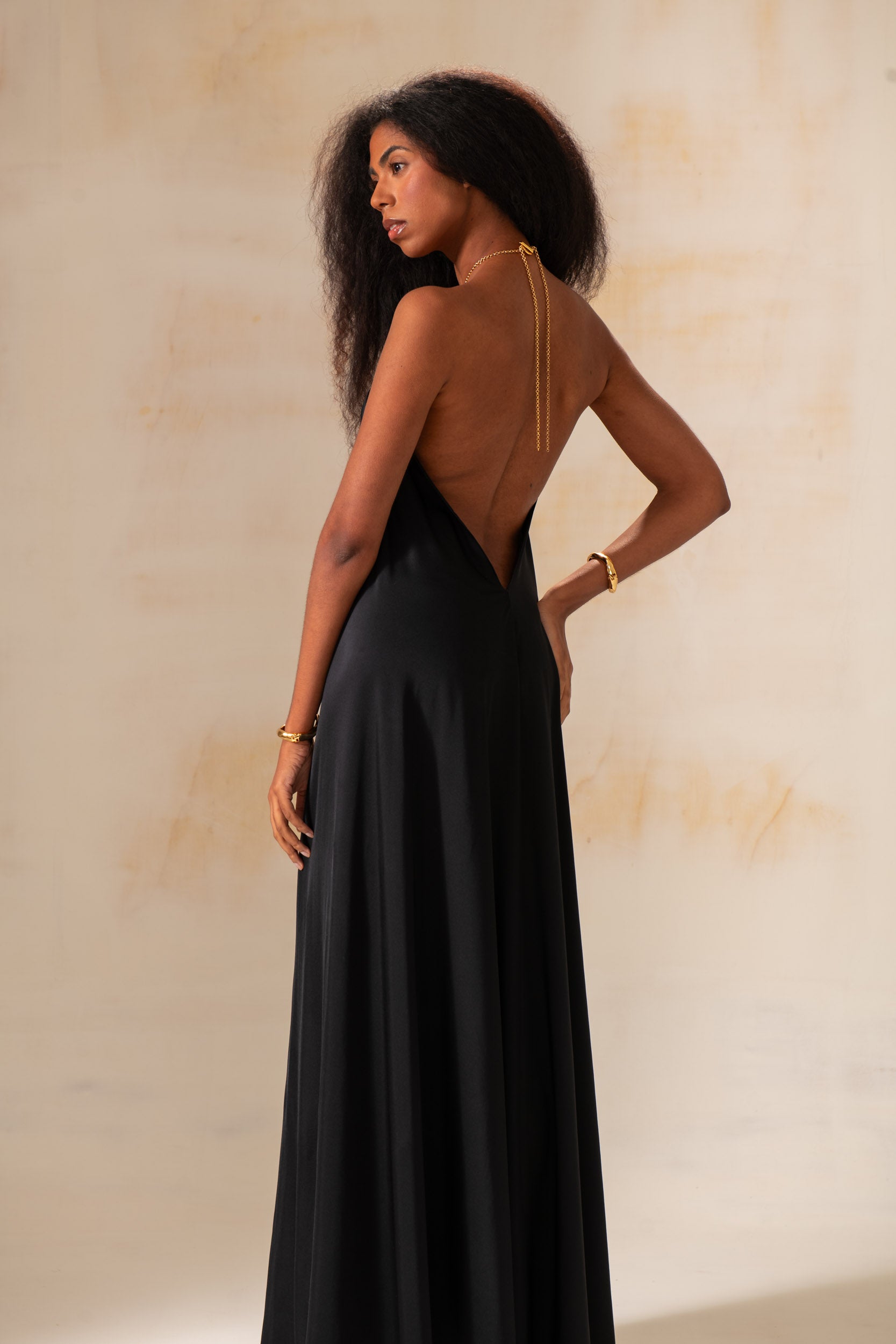 Model wearing a halter maxi dress with gold ring neckline and open back in a resort-style photoshoot