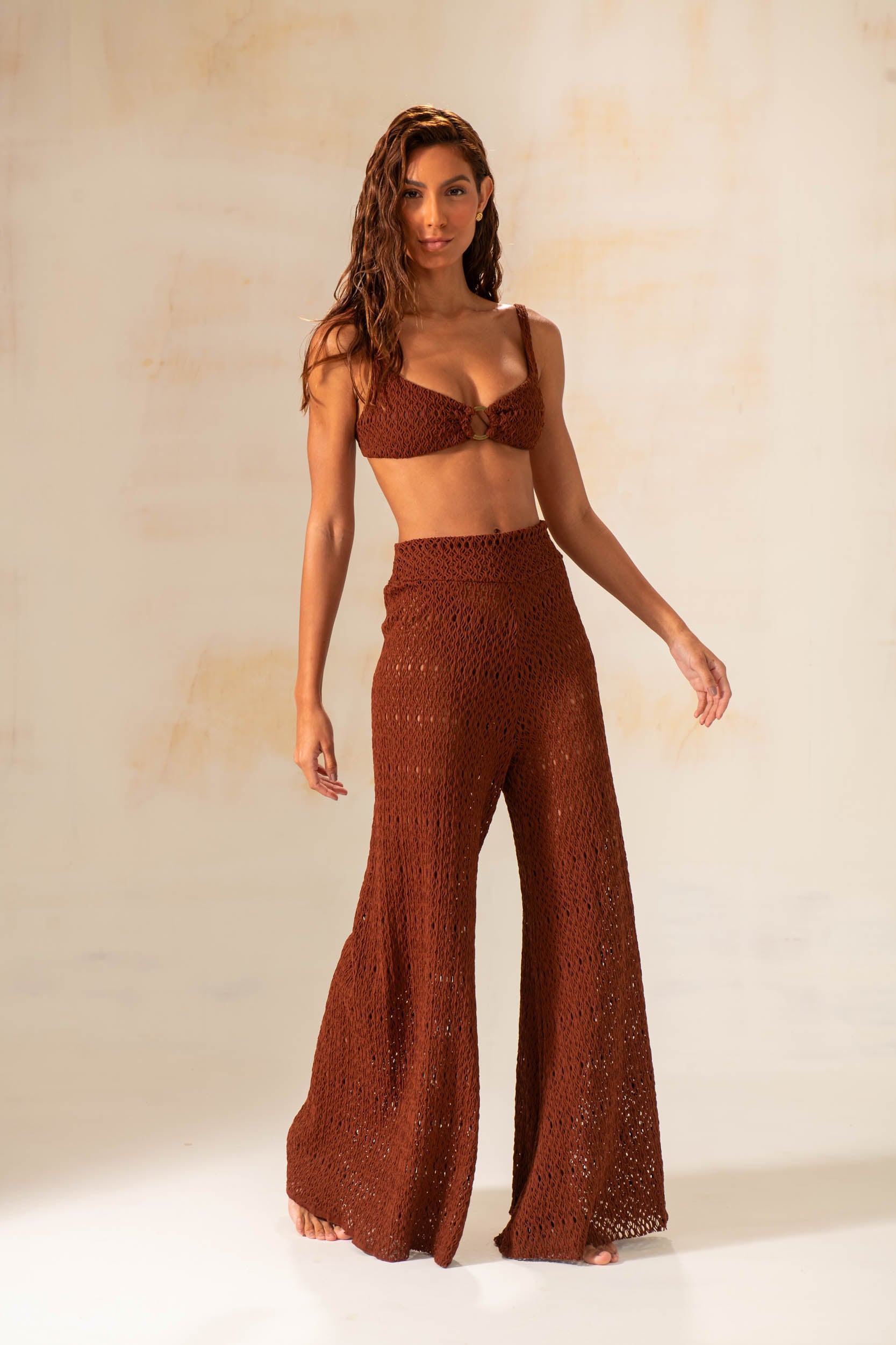 Model wearing handmade crochet wide-leg pants in natural and rust tones, styled as beach cover-up with matching tops.